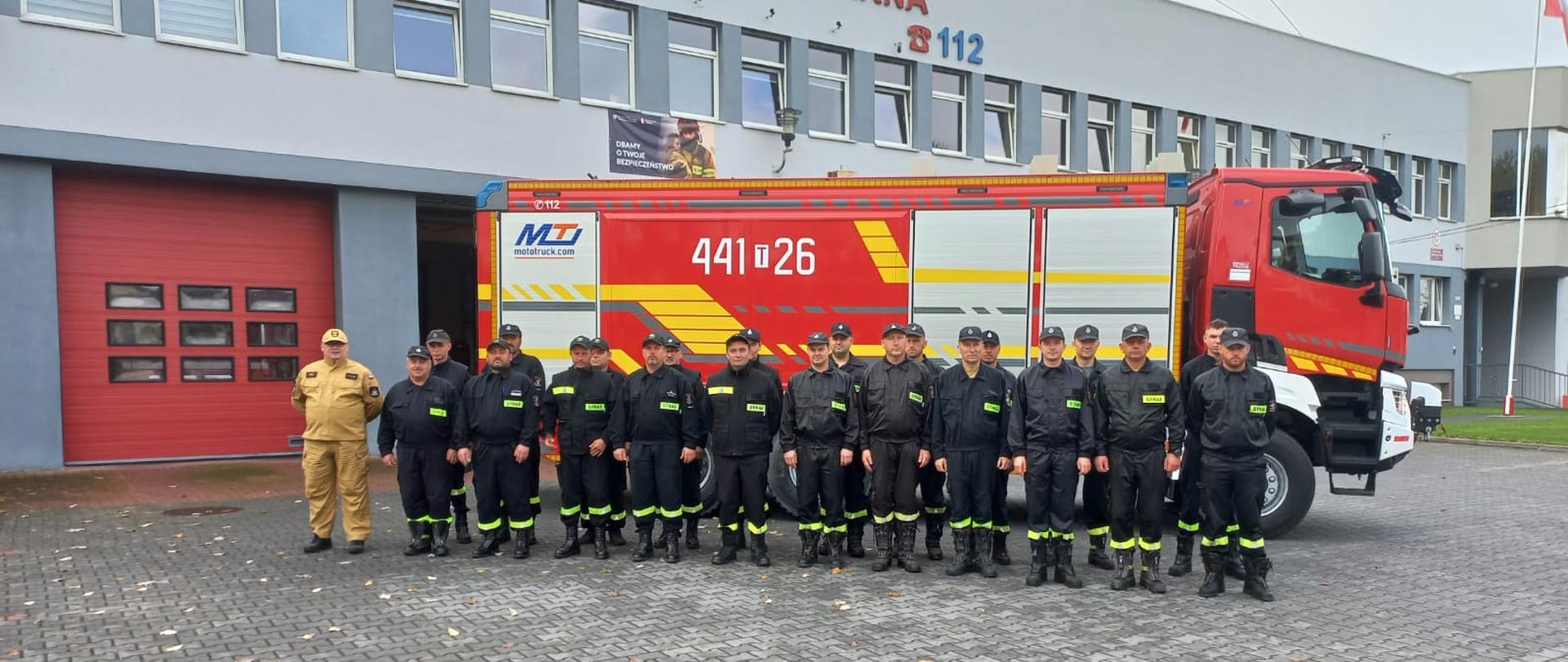 Strażacy stojący w ubraniach koszarowych przed budynkiem jednostki KP PSP w Opatowie. 