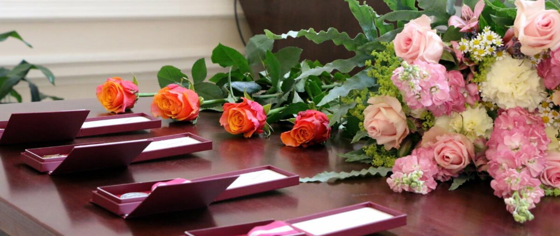 Na stole umieszczone odznaczenia państwowe w etui. Obok wiązanki kwiatów