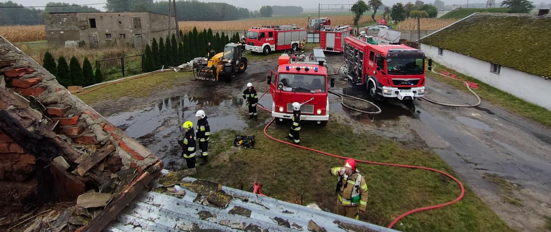 Samochody strażackie stoją na drodze. Węże leżą na ziemi.