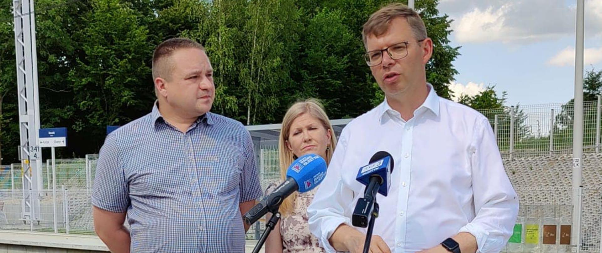 Wojewoda przemawia na stacji kolejowej a za nim stoją dwie osoby 