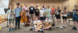 Kilkanaścioro dzieci stoi lub siedzi na scenie ze swoimi instrumentami.