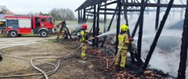 Dwóch strażaków gaszących stodołę za pomocą linii gaśniczych.