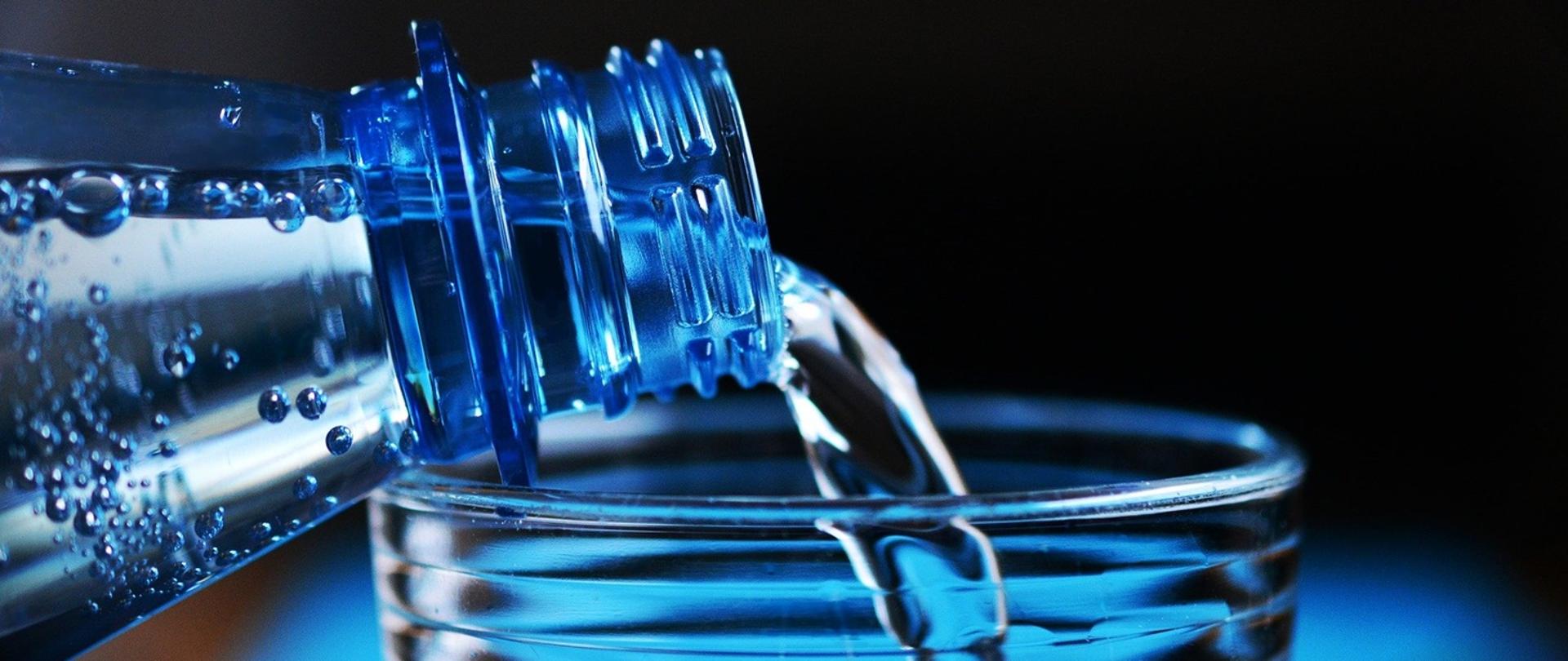 zdjęcie przedstawia moment nalewania wody z butelki do szklanki