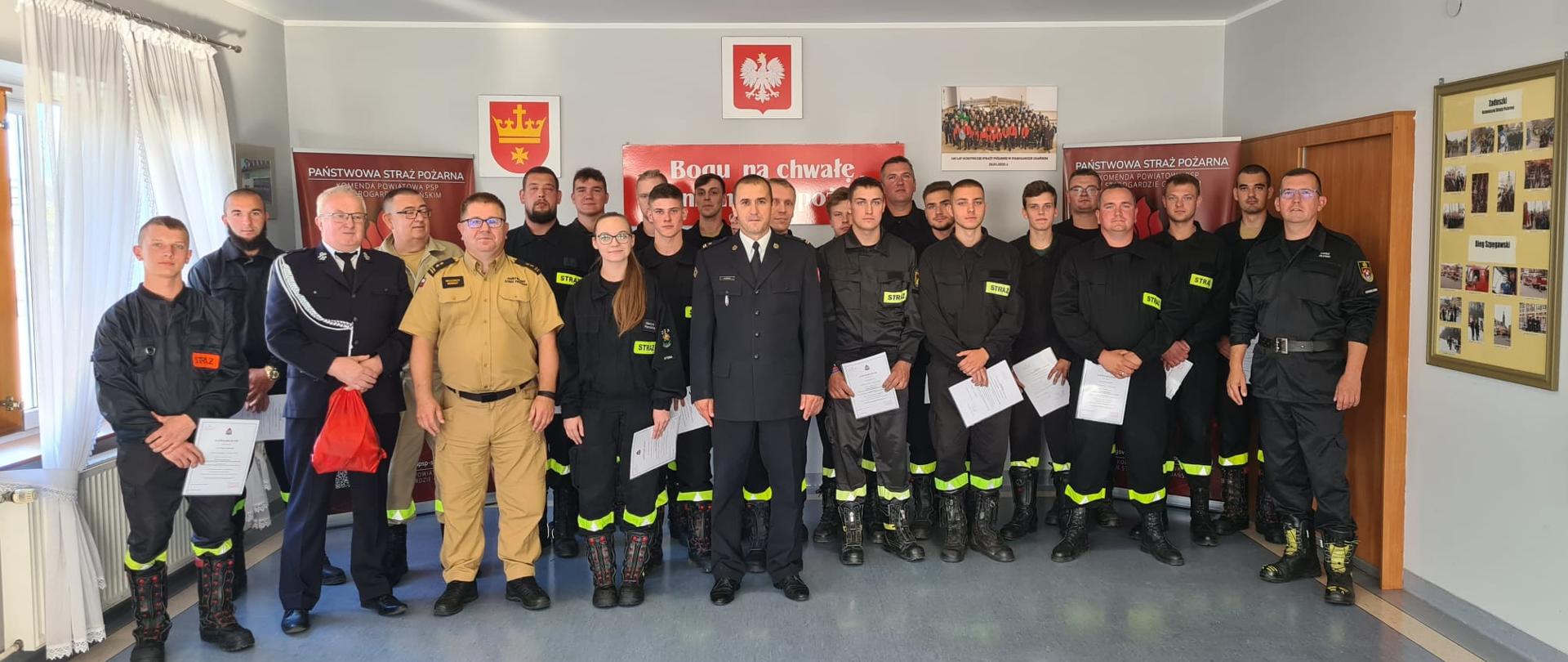 Zdjęcie przedstawia uczestników kursu wraz z zaproszonymi gośćmi: zastępca pomorskiego komendanta wojewódzkiego PSP bryg. Wojciech Berent, wiceprezes Zarządu Oddziału Powiatowego ZOSP RP w Starogardzie Gdańskim dh Łukasz Zblewski i prezes Zarządu Gminnego ZOSP RP w Osiecznej dh Jerzy Krzemiński. Gospodarzem uroczystości był zastępca komendanta powiatowego PSP w Starogardzie Gdańskim mł. bryg. Tomasz Nowak.