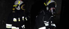 Widok z przodu. Dwóch strażaków OSP w ubraniach specjalnych, hełmach i aparatach ochrony dróg oddechowych w czasie ćwiczeń w piwnicy JRG Wadowice.