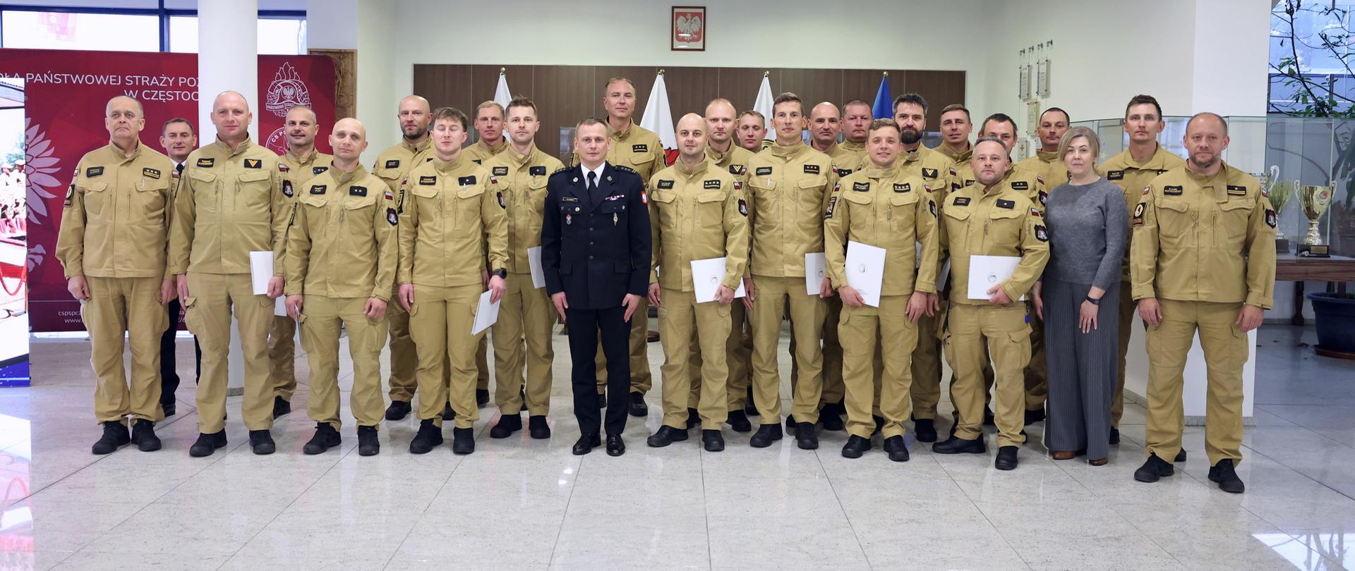 Pamiątkowe zdjęcie grupowe funkcjonariuszy PSP będących uczestnikami szkolenia z zakresu kierowania działaniem ratowniczym na poziomie interwencyjnym (20 osób) w towarzystwie Zastępcy Komendanta CS PSP, kobiety oraz czterech funkcjonariuszy CS PSP