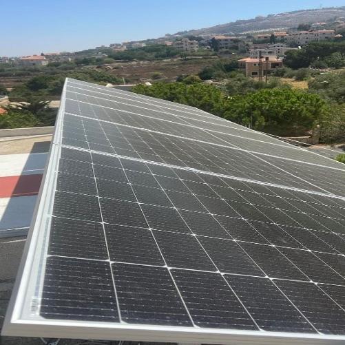 Na tle domów rozsianych na wzgórzu widać system fotowoltaiczny zainstalowany na dachu budynku