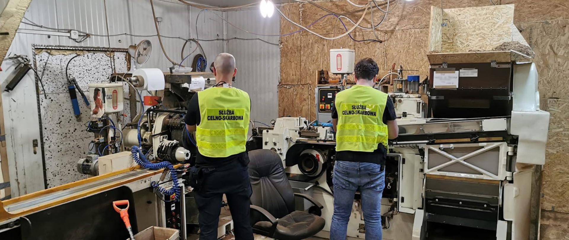 Funkcjonariusze Służby Celno-Skarbowej przy maszynach do produkcji papierosów.