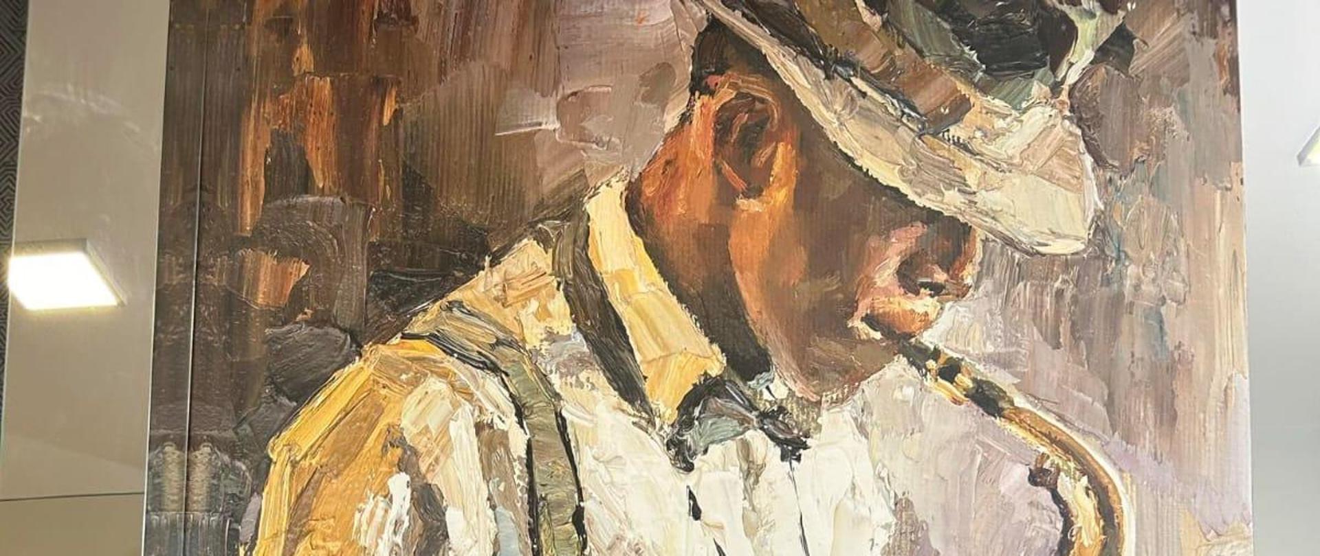 Po środku uczennica trzymająca flet, a po jej bokach dwie nauczycielki. W tle widoczny obraz przedstawiający mężczyznę grającego na saksofonie.