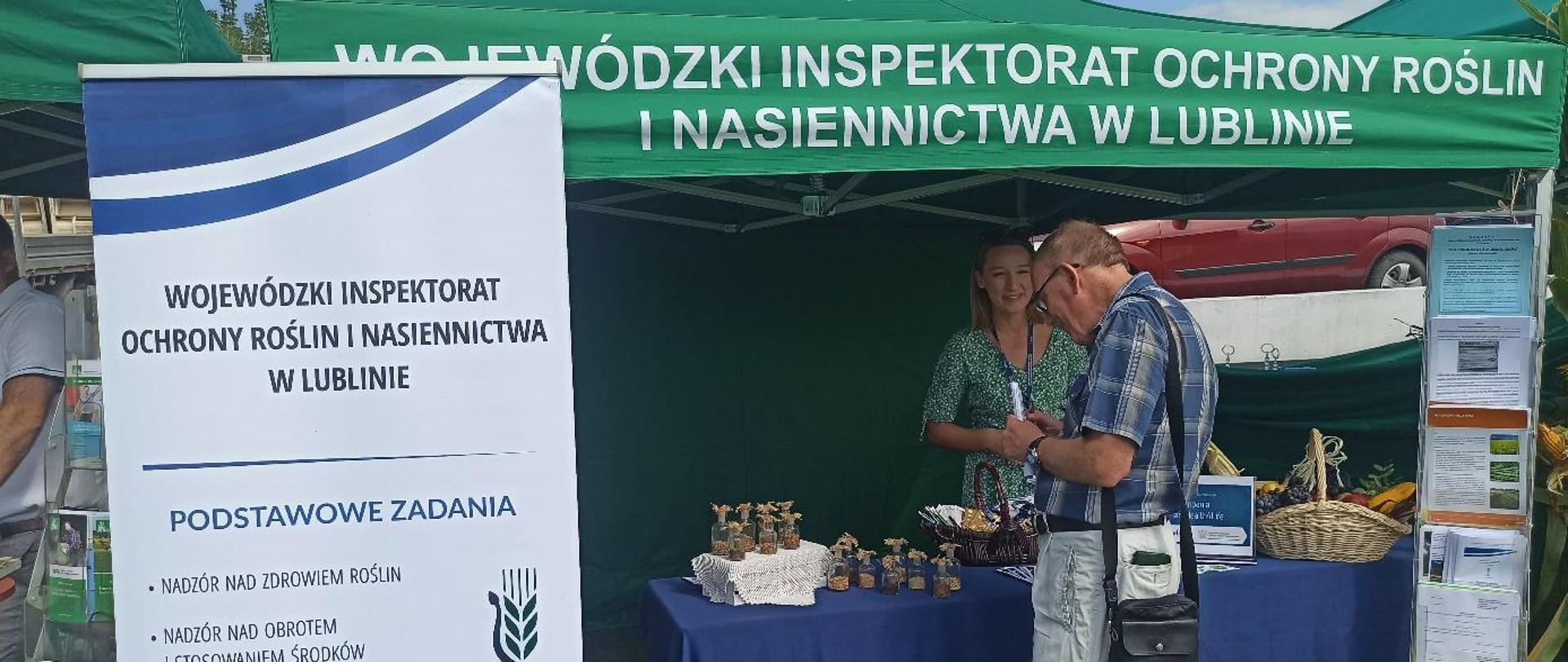  Pracownik WIORiN w Lublinie rozmawia z uczestnikiem dożynek na temat działalności Inspekcji przy stoisku informacyjno-promocyjnym