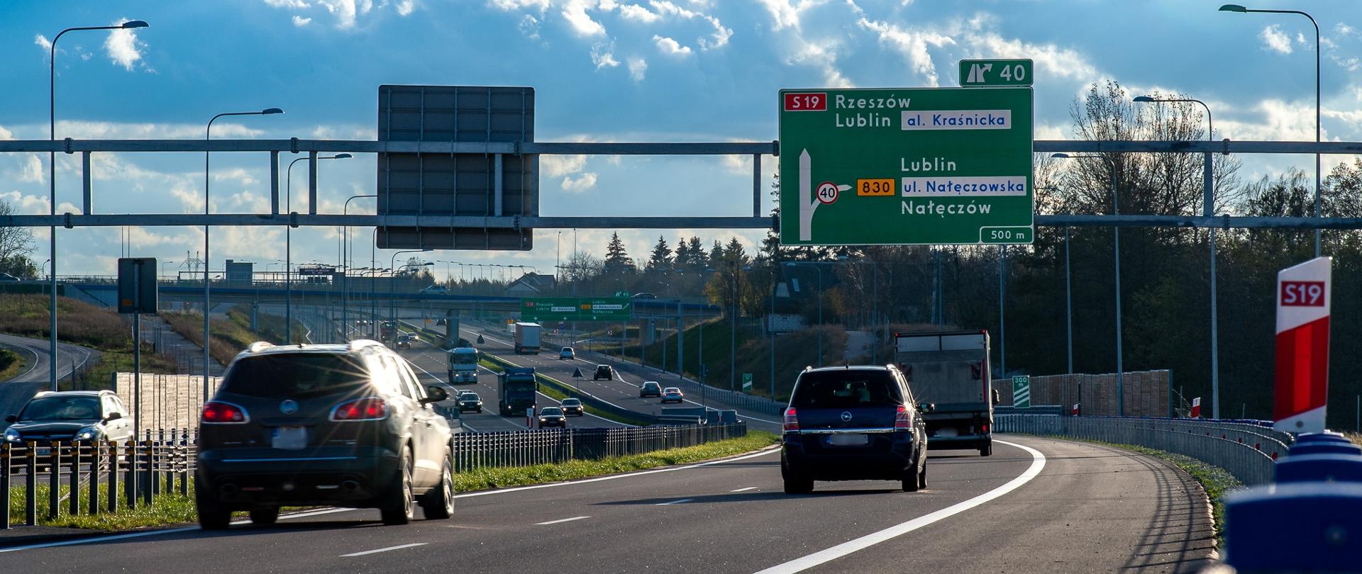 Ruch samochodowy na drodze ekspresowej S19; nad jezdnią widoczne tablice kierunkowe informujące o zjazdach w kierunku Lublina, Rzeszowa i Nałęczowa.