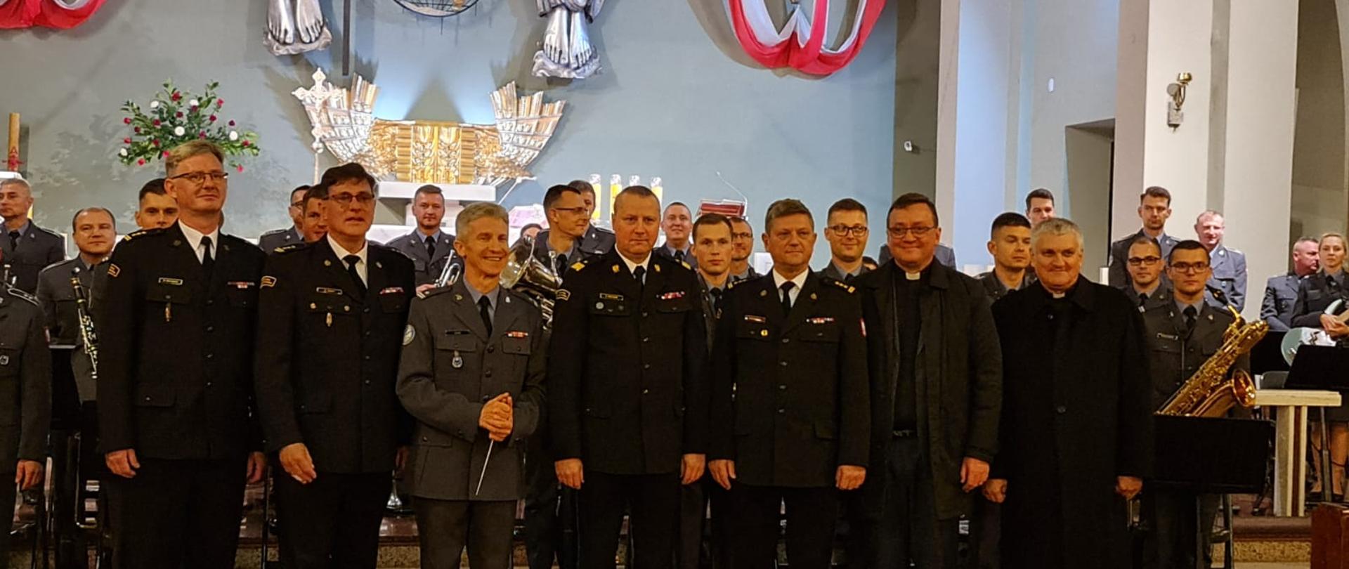 zdjecie grupowe orkiestry, strażaków i księży , w tle ołtarz