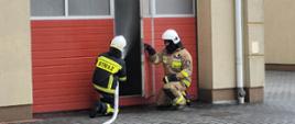 Zdjęcie przedstawia dwóch strażaków podczas ćwiczenia wejścia do pomieszczenia, w którym rozwija się pożar.