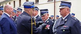 Widok z boku. Zastępca Komendanta Wojewódzkiego PSP dekoruje medalami za zasługi dla społeczności lokalnej druhów OSP. 