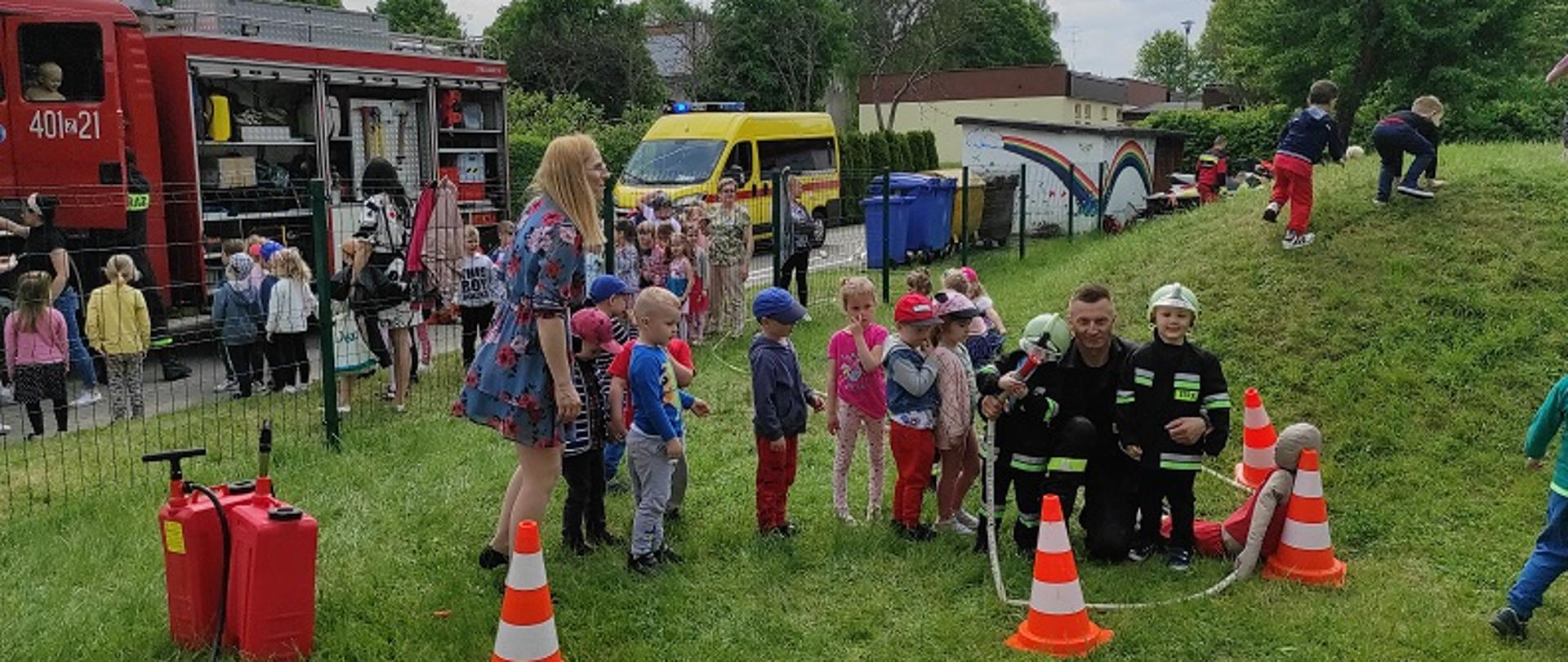 Dzień Dziecka w przedszkolu „Niezapominajka”. Na zdjęciu klęczący strażak w otoczeniu przedszkolaków podczas konkurencji lania wody z prądownicy strażackiej