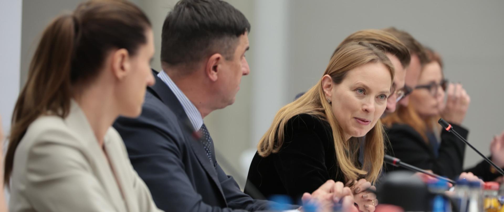W sali konferencyjnej grupa osób siedzi przy stole. Wśród nich minister Katarzyna Pełczyńska-Nałęcz.