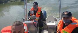 Zdjęcie przedstawia strażaków płynących łodzią, którzy przeszukują obszar wodny na rzece Wisła 