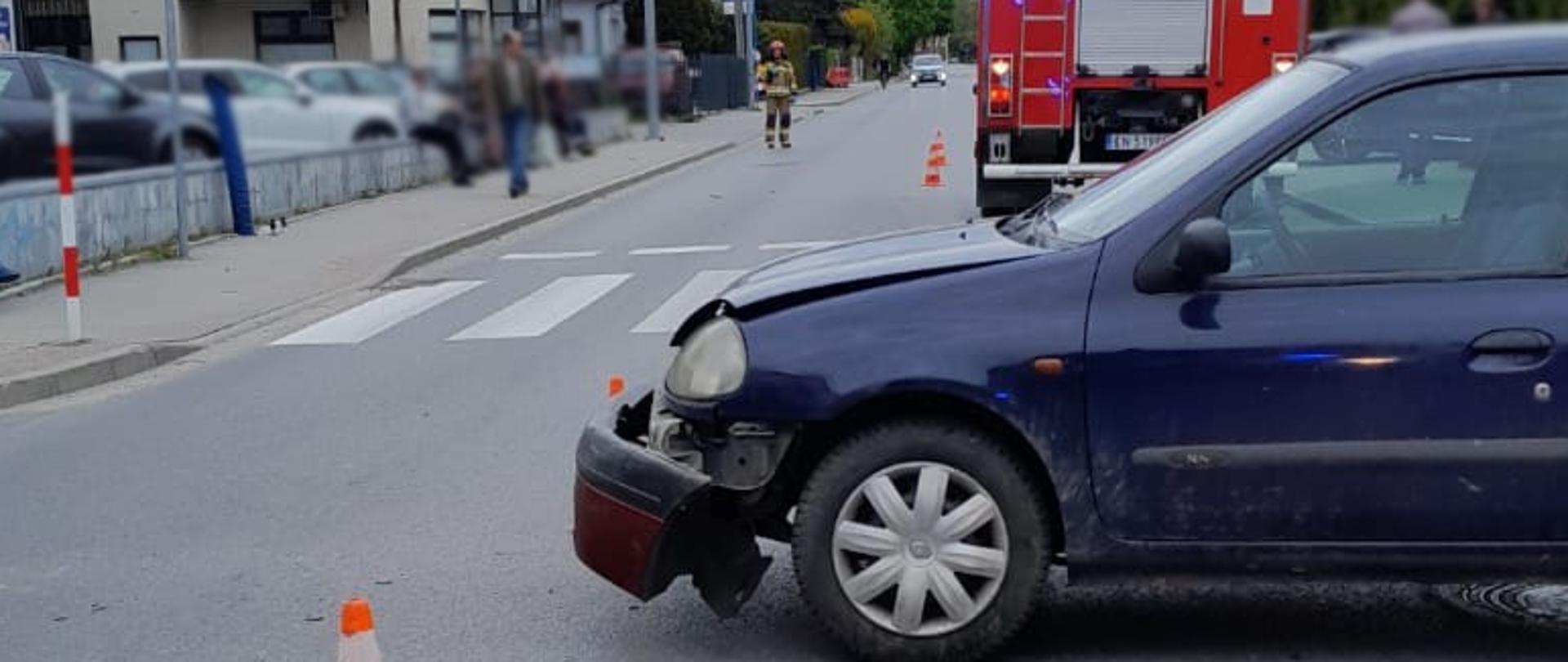 Fragment rozbitego samochodu a w tle samochód pożarniczy