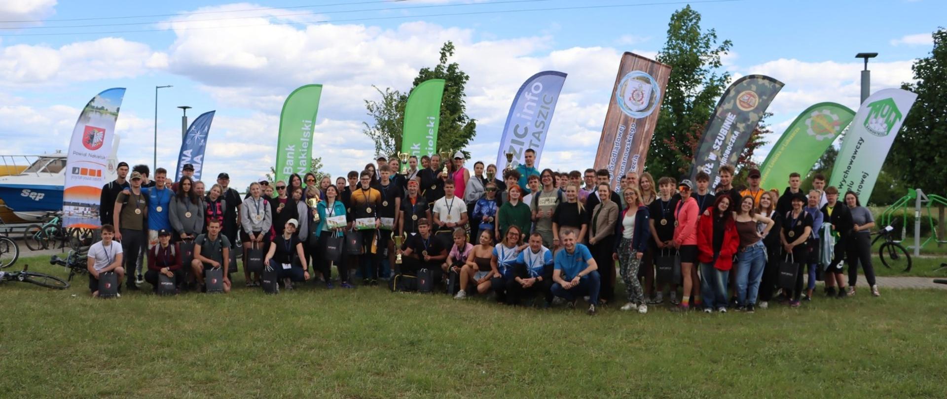 Grupowe zdjęcie uczestników SAR Schools Adventure Race na tle banerów sponsorów i organizatorów.