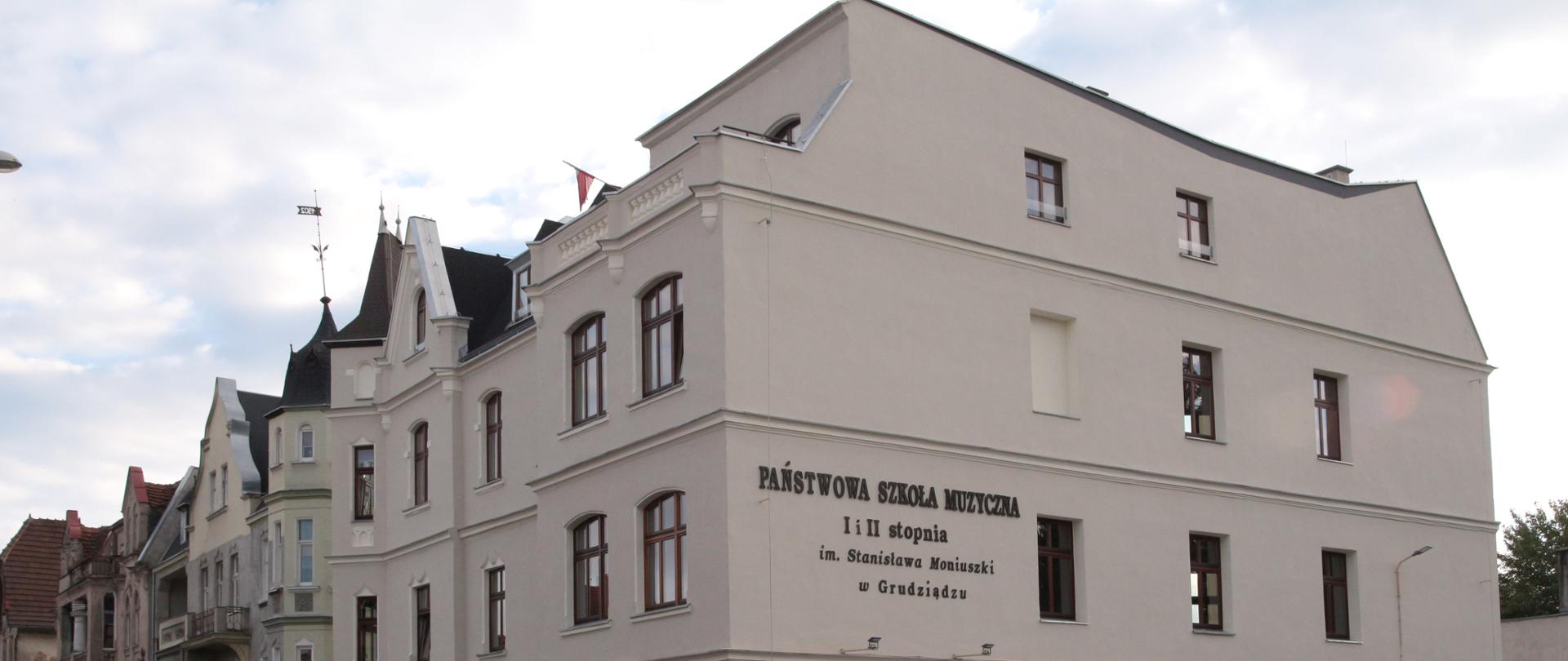 Zdjęcie przedstawia trzykondygnacyjną kamienicę w kolorze beżowym z napisem na ścianie Państwowa Szkoła Muzyczna I i II stopnia im. Stanisława Moniuszki w Grudziądzu