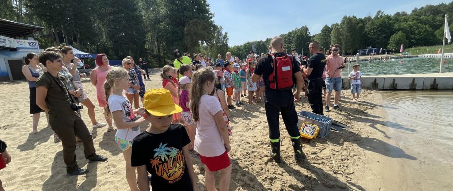 Na zdjęciu widnieją dzieci w trakcie akcji prewencyjnej na plaży, która została zorganizowana przez strazaków. 