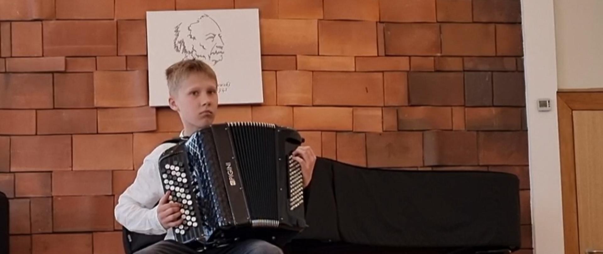 Chłopiec gra na akordeonie, w tle stoi fortepian.
