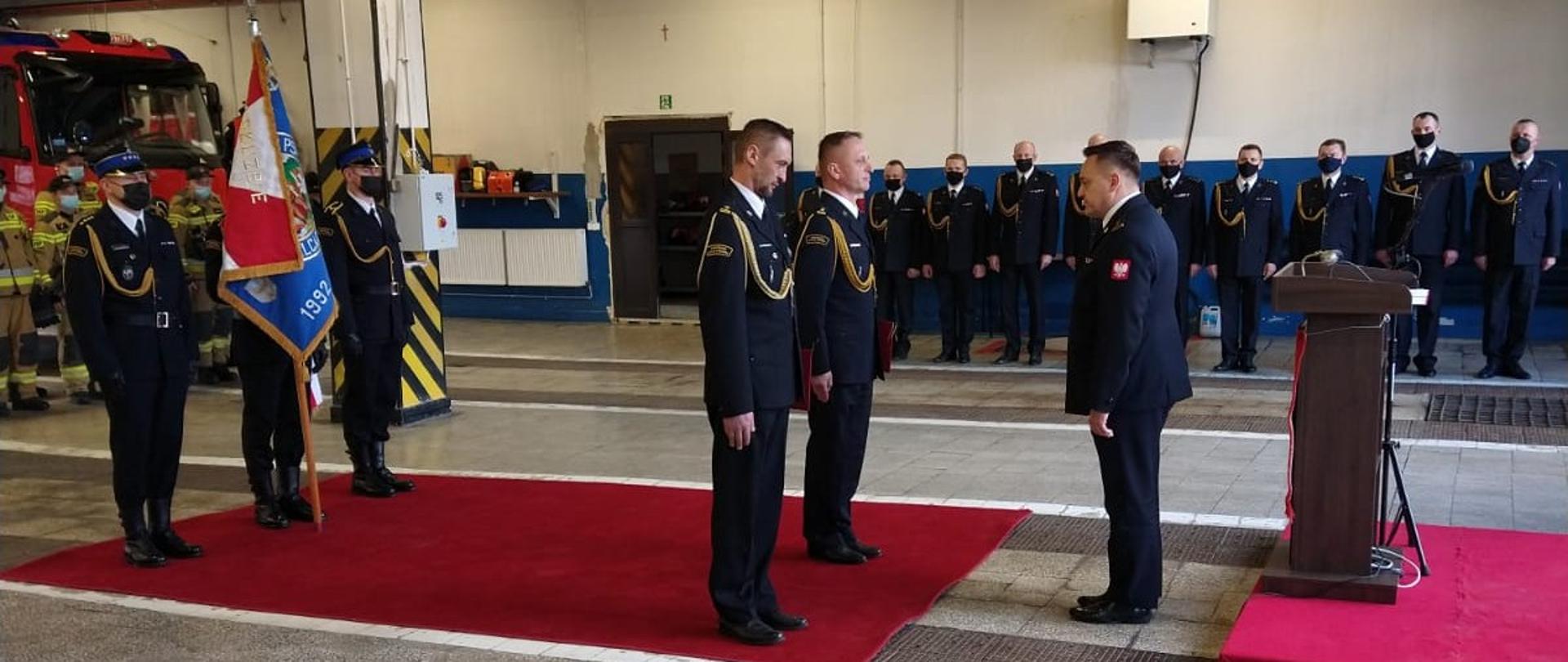 Na zdjęciu znajdują się strażacy oraz poczet sztandarowy w garażu