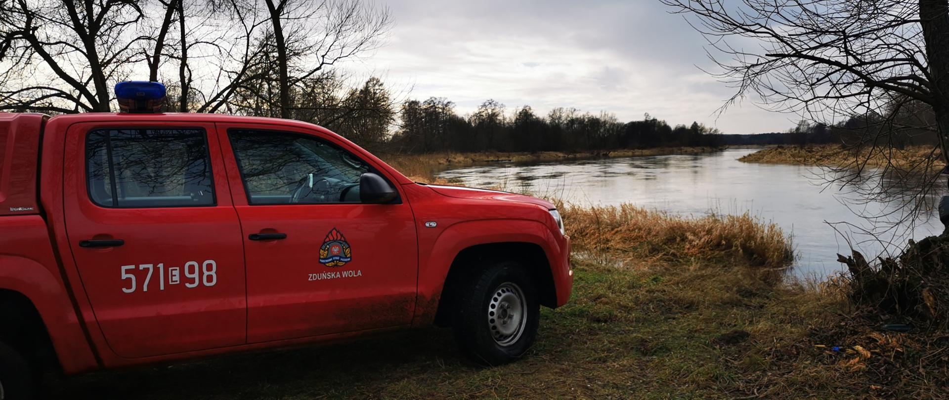 Na zdjęciu widoczny bok samochodu operacyjnego z JRG PSP w Zduńskiej Woli o numerach 571E98 w kolorze czerwonym stojący przy rzece Warcie. 