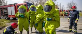Strażacy zabezpieczeni w ubranie gazoszczelne ochrony chemicznej przygotowują się do wykonania zadania polegającego na uszczelnieniu zbiornika z którego wycieka substancja niebezpieczna. 