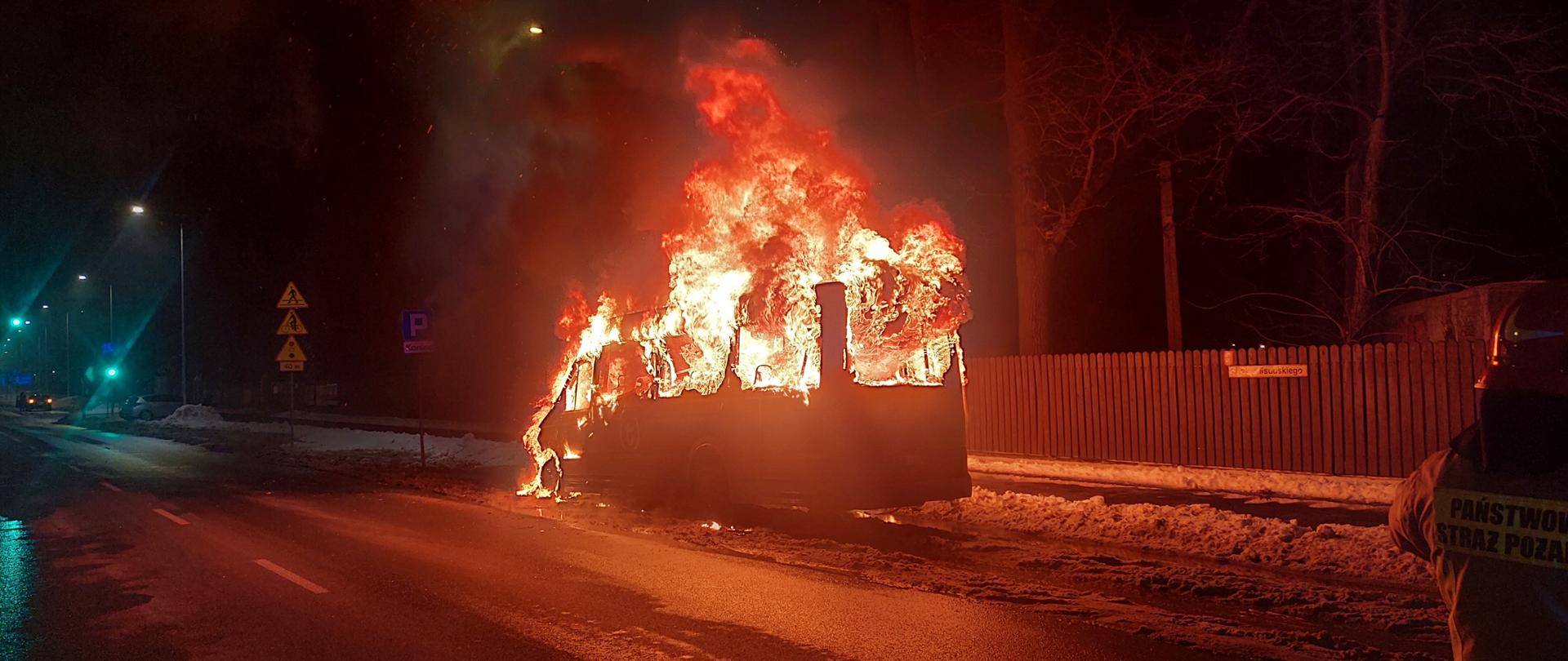 Zdjęcie przedstawia działania gaśnicze podczas pożaru autobusu. Na zdjęciu widoczny jest w pełni palący się pojazd.