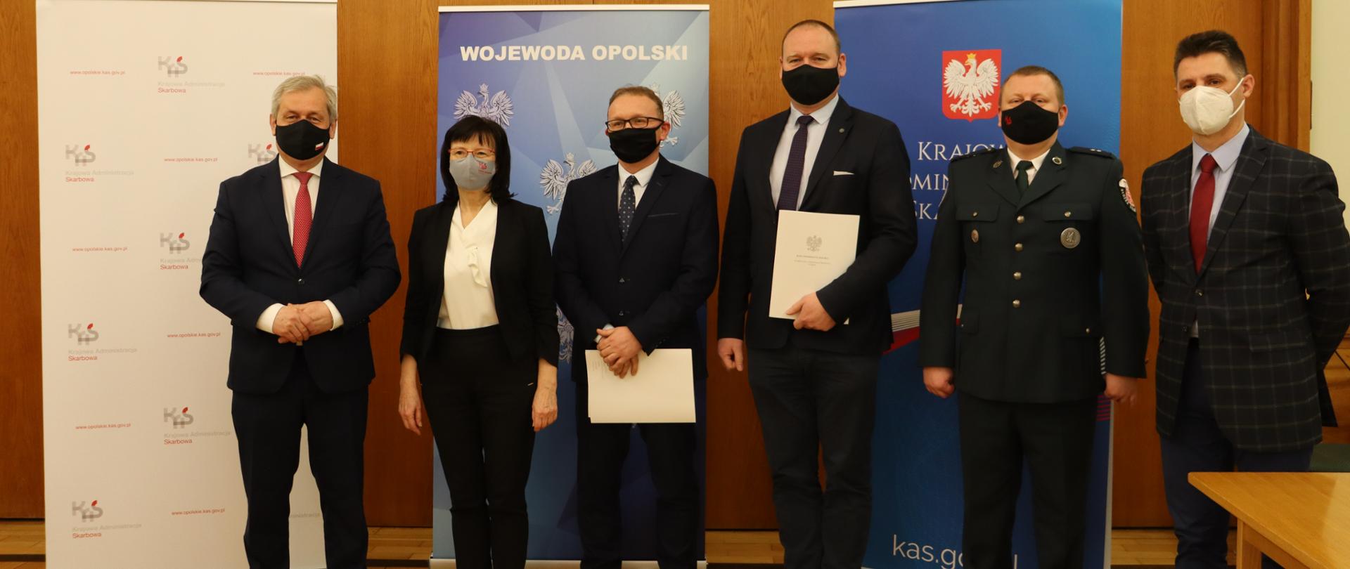 Na zdjęciu osoby, które podpisały porozumienie. W tle ścianka z logo wojewody opolskiego. Wojewoda stoi na zdjęciu po lewej stronie - wszyscy pozują do fotografii