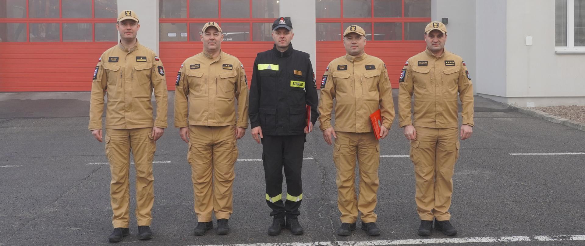 Komendanci Powiatowi, dowódca JRG wraz z funkcjonariuszami awansowanymi na wyższe stopnie służbowe pozują do zdjęcia w tle budynek Komendy Powiatowej Państwowej Straży Pożarnej w Opocznie. 