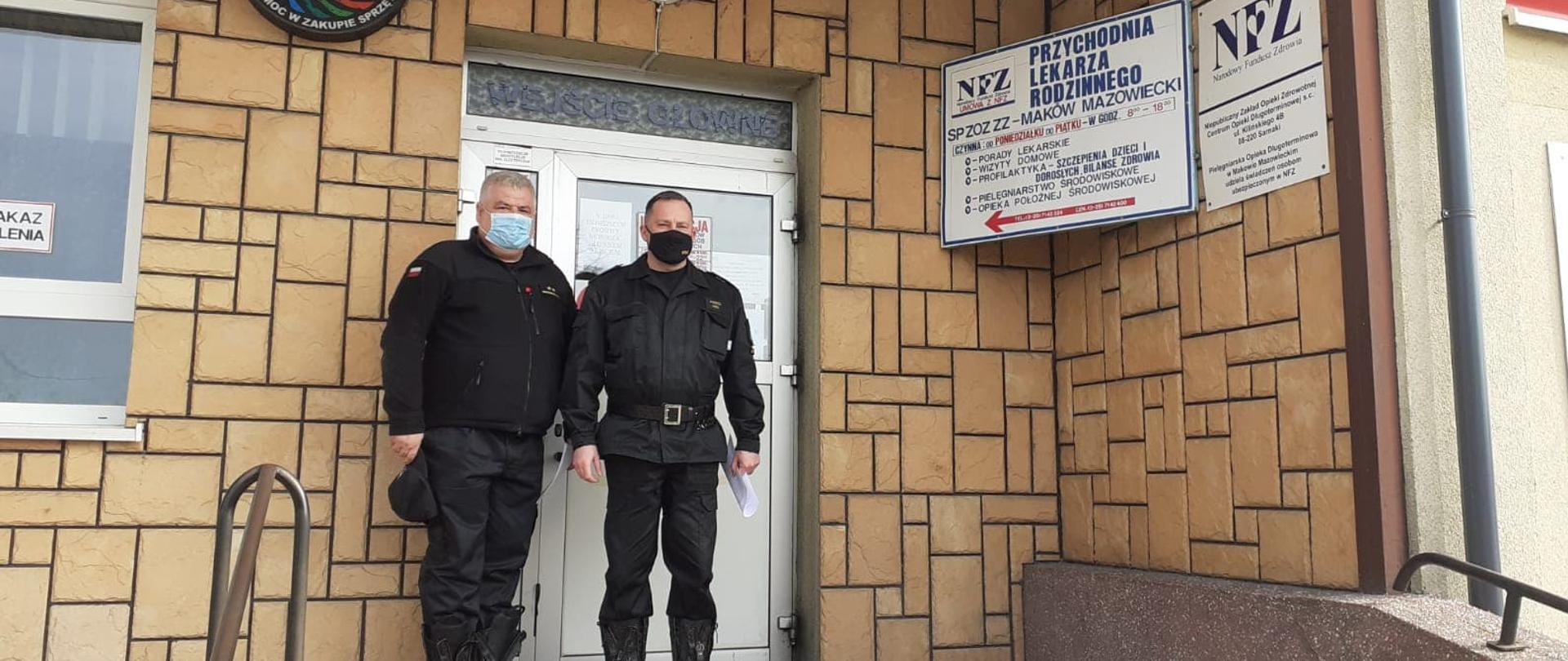 Dwóch strażaków stoi przed drzwiami wejsciowymi szpitala.