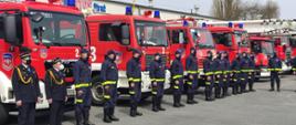 Strażacy Lotos Straż Sp. z o.o. stoją na tle samochodów ratowniczo-gaśniczych.