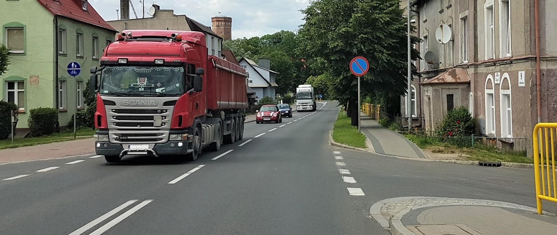 Zdjęcie przedstawia drogę krajową nr 25 w Człuchowie z ruchem pojazdów i zabudową mieszkaniową.