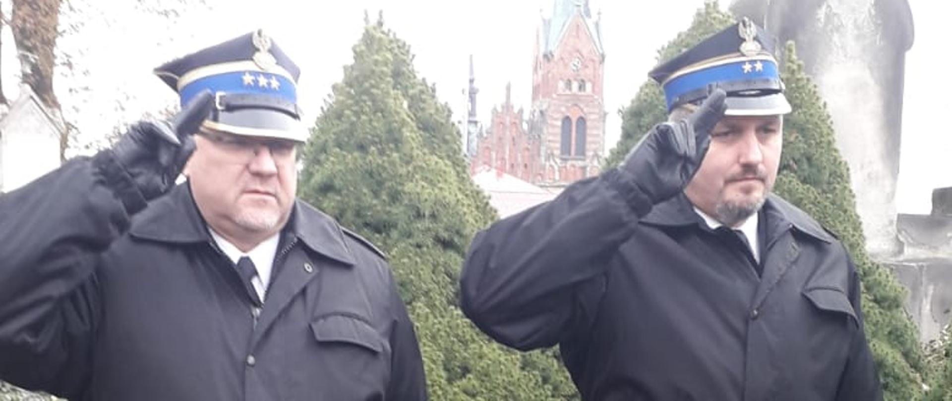 Na zdjęciu widać dwóch funkcjonariuszy oddających honor przy grobie 