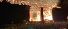 Widoczne miejsce zdarzenia płonący budynek stodoły ze zniszczoną konstrukcją dachu widać dym i płomienie.