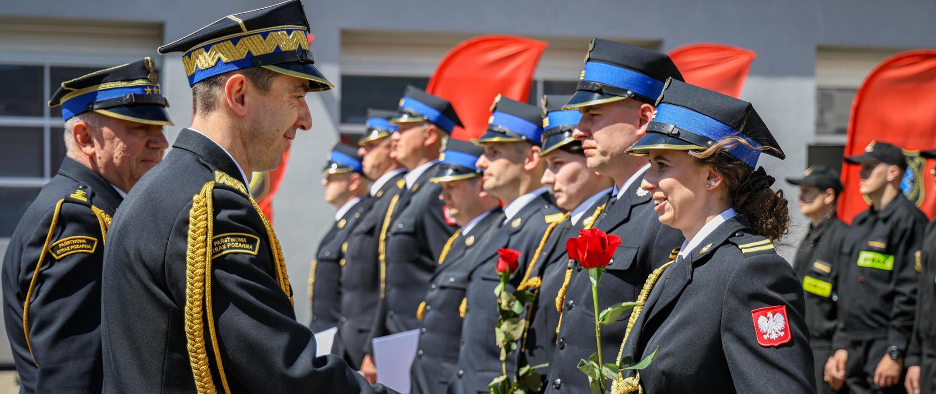 Komendant główny i miejski PSP wręcza odznaczenia strażakom, dwie funkcjonariuszki trzymają w dłoniach czerwone róże