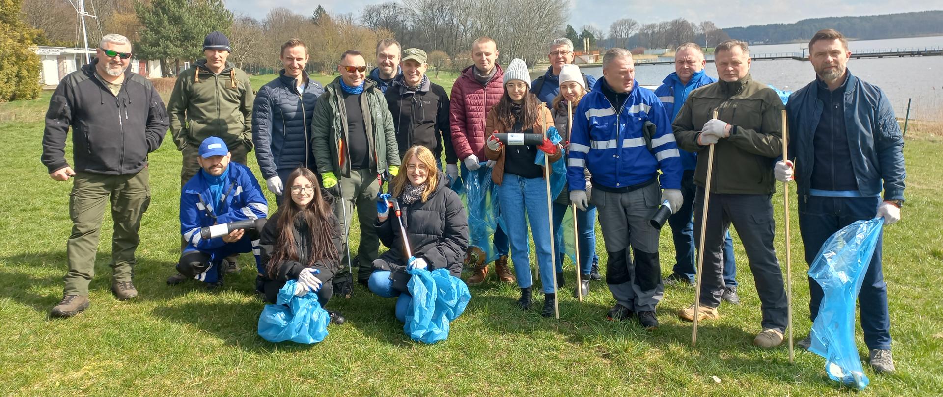 Grupa pracowników lubelskich Wód Polskich i PZW Okręg w Lublinie na tle Zbiornika Zemborzyckiego. W rękach trzymają worki na śmieci.