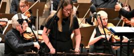 Zdjęcie przedstawiające ksylofonistkę - Alicję Michalak na scenie filharmonii. W tle orkiestra symfoniczna. 
