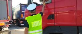 Na pierwszym planie umundurowany inspektor lubuskiej ITD stoi obok kabiny ciężarówki i kontroluje stan trzeźwości kierującego. W tle widoczny tył dwóch zestawów ciężarowych.