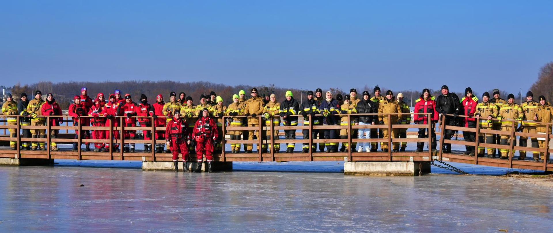 grupa osób w mundurach stojących na pomoście na zamarzniętym jeziorze