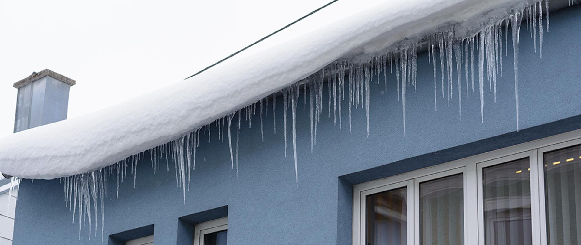 Śnieg na dachu i zwisające sople lodu.