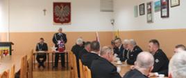 Jeden ze strażaków przemawia na stojąco, pozostali siedzą przy stołach