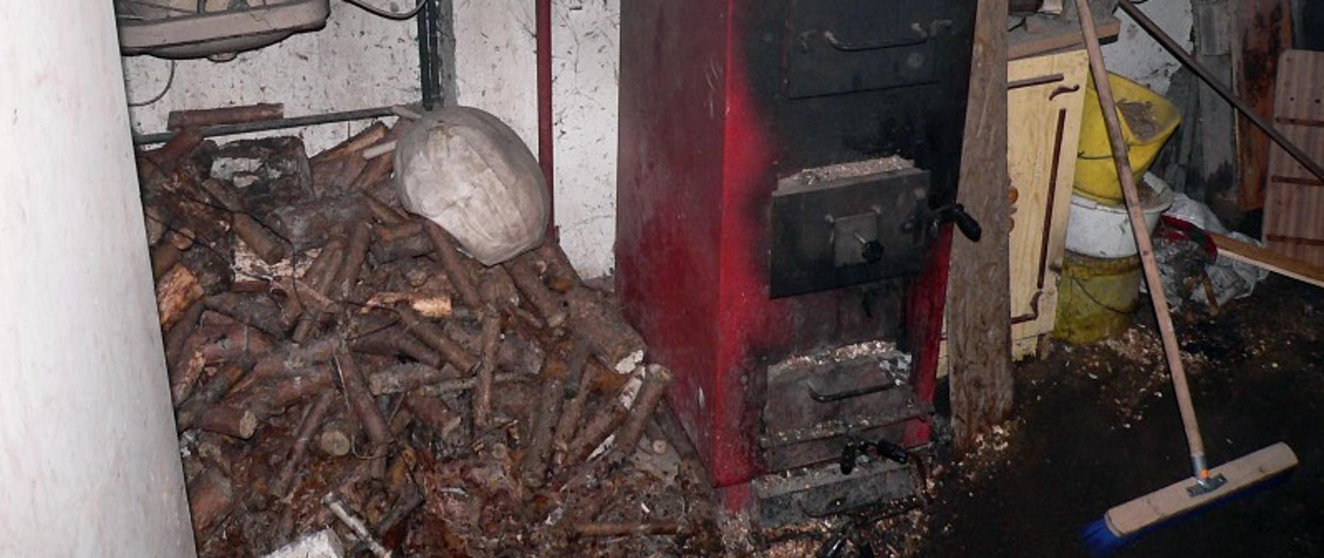 Piec centralnego ogrzewania na paliwo stałe obok składowane drewno i różnego typu przedmioty.