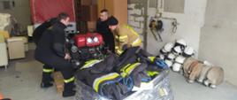 Sprzęt pożarniczy dla ukraińskich strażaków. Komenda Powiatowa PSP w Rawiczu. Strażacy przygotowują do transportu zebrany sprzęt. Na europaletę stawiają przywieziona motopompę. Na pierwszym planie ubrania specjalne, obok węże i hełmy strażackie.