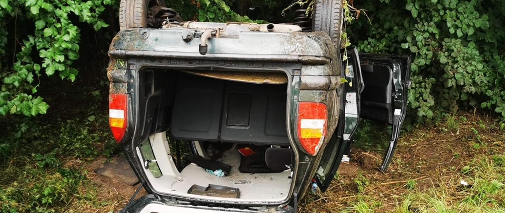 Widok na tył samochodu osobowego leżącego na dachu. Otwarta klapa bagażnika