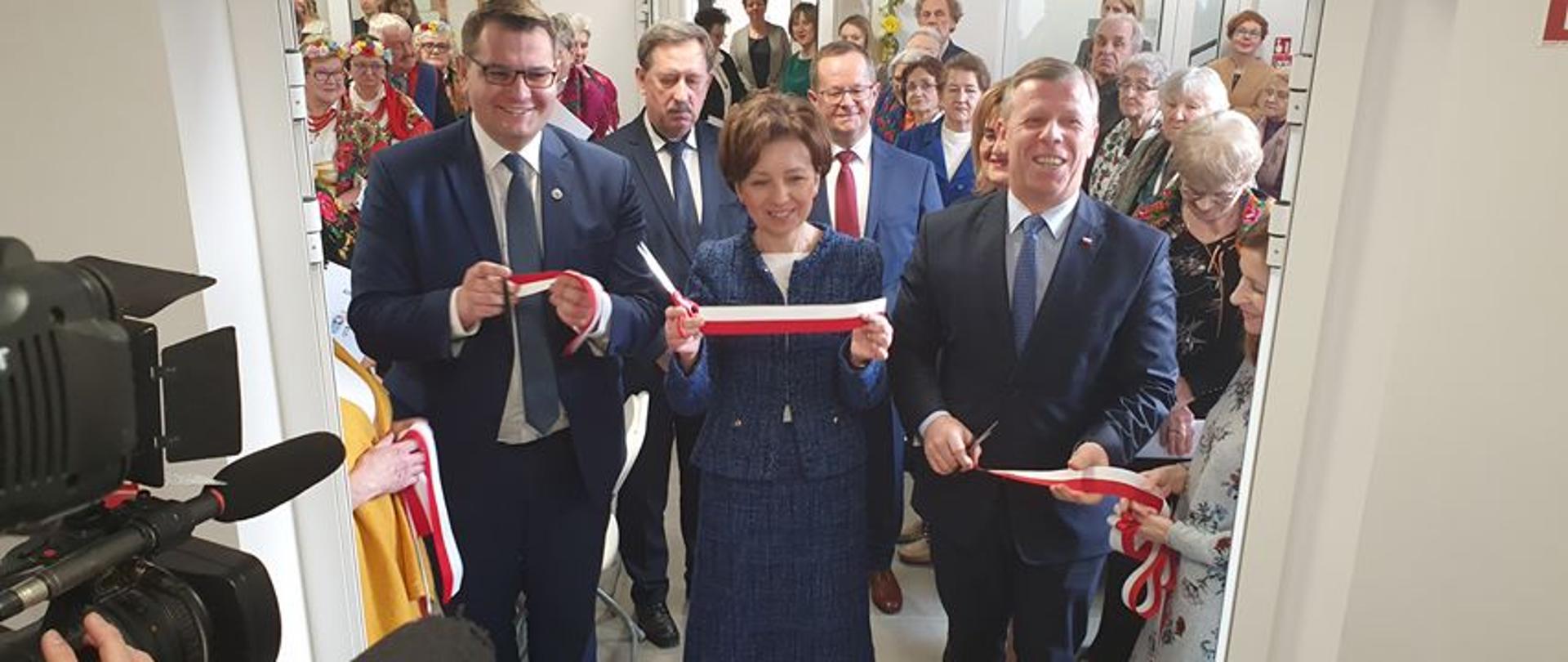 Otwacie domu Senior plus w Myślenicach. Minister Marlena Maląg pokazuje fragment wstęgi po przecięciu. W tle seniorzy, cześć z nich w ludowych strojach.