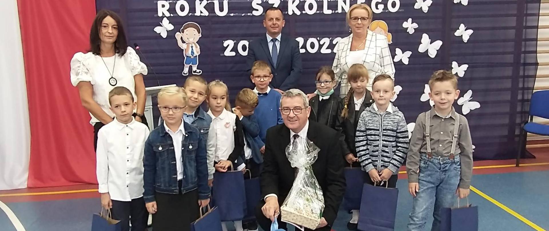 na zdjęciu widoczne dzieci z ministrem W. Murdzkiem wraz z nauczycielami, którzy biorą udział w inauguracji roku szkolnego na sali gimnastycznej w szkole