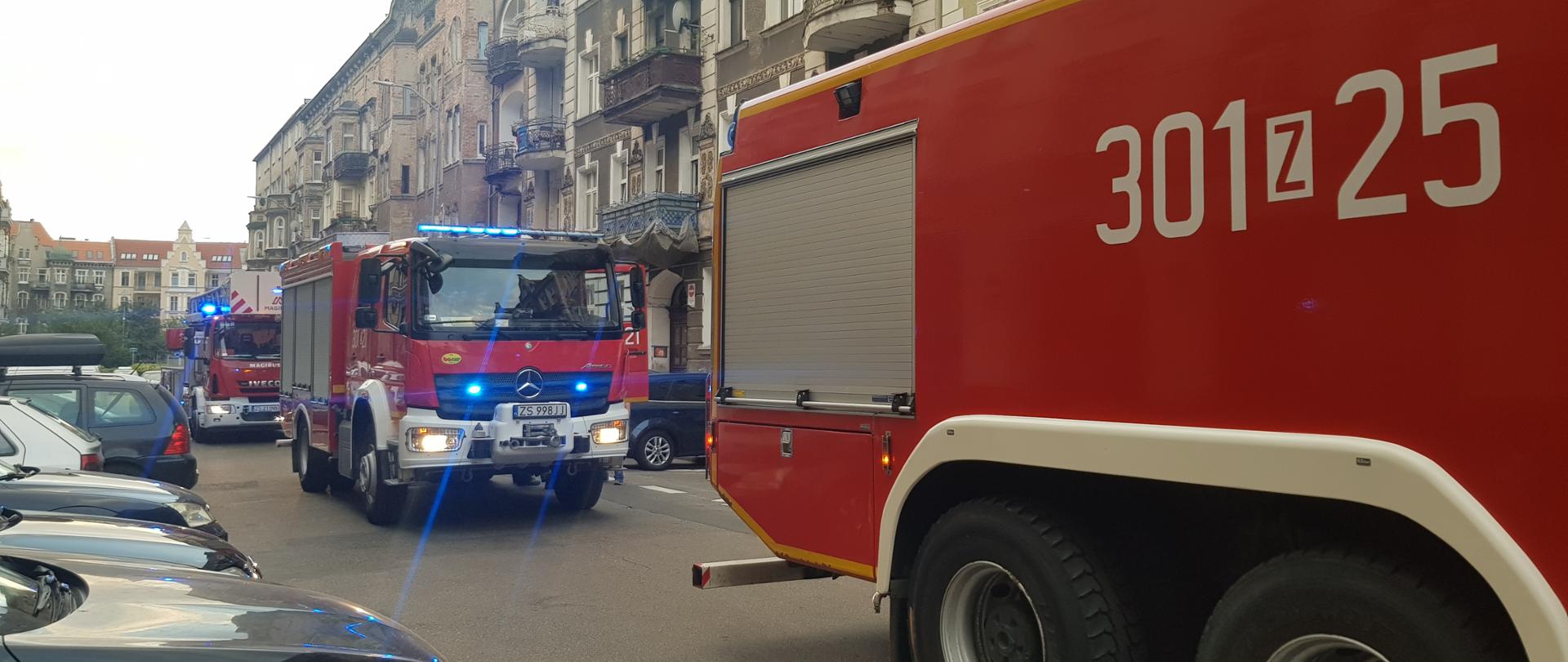 W centralnej części zdjęcia wóz bojowy straży pożarnej, poprzedza go ciężki wóz bojowy a za nim stoi drabina mechaniczna 